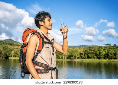 Young Asian man backpacker traveling in the forest. Male traveler holds a bottle of water. Healthy hiker drinking water in nature hike. Young man living active life, fun and smile. - Powered by Shutterstock