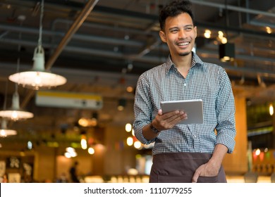 Young Asian Man Barista Holding Tablet And Looking Forward While Standing At Inside Modern Restaurant Cafe Shop Background For SME New Small Business Lifestyle And Franchise Investment Concept