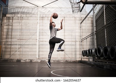 young asian man basketball player attempting a dunk on outdoor court - Powered by Shutterstock