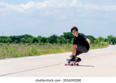 A Young Asian Man In A Black Shirt And Pants Is Playing Figure Skating On A Rural Road. In The Sun On A Bright Day, Play Surf Skate