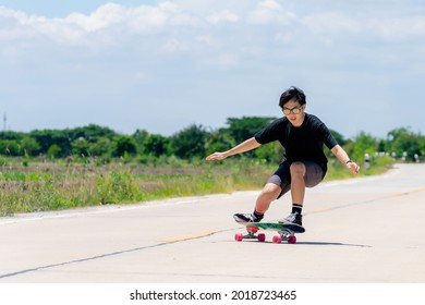 A Young Asian Man In A Black Shirt And Pants Is Playing Figure Skating On A Rural Road. In The Sun On A Bright Day, Play Surf Skate