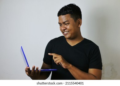 Young Asian Man In Black Shirt Holding Laptop And Pointing At Screen With Right Hand And Looking Happy