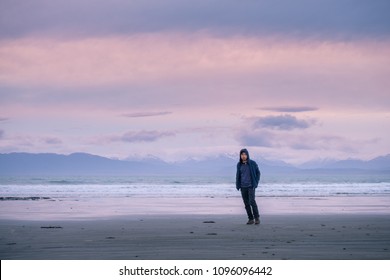 A young Asian man with blue jacket standing on the beach at sunset with dusk scene. snow mountain with cloudy background.