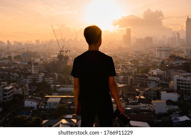 Young asian man with camera standing on top of building and view of sunrise on Bangkok city in Thailand