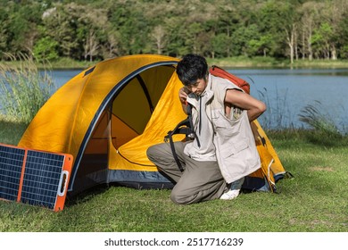 Young Asian man camper preparing to hike with backpack near tent and solar panels by lake in scenic nature setting - Powered by Shutterstock