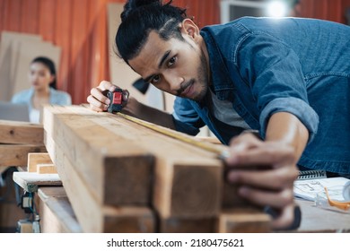 Young Asian man Carpenter uses a tape measure to measure wood on the workbench in woodcraft carpentry workshop. 