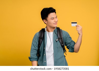 Young Asian Man In Casual Wear Holding Credit Card On Yellow Background