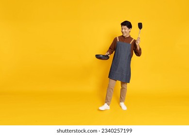 Young Asian man chef wearing kitchen apron cooking and holding pan and spatula isolated on yellow background, Full body composition - Powered by Shutterstock