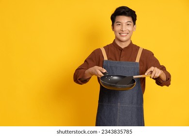 Young Asian man chef wearing kitchen apron cooking and holding pan and spatula isolated on yellow background - Powered by Shutterstock