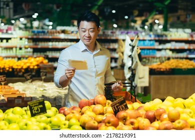 Young Asian Man Chooses And Picks In Eco Bag Apple Fruit Or Vegetables In The Supermarket. Male Customer Standing A Grocery Store Near The Counter Buys And Throws In A Reusable Package In Market