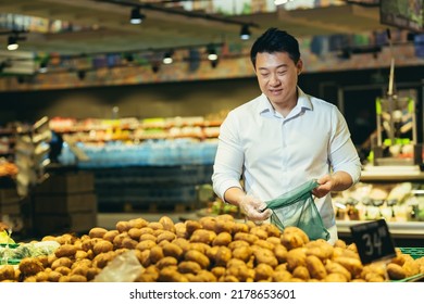 Young Asian Man Chooses And Picks In Eco Bag Vegetables Potato Or Fruits In The Supermarket. Male Customer Standing A Grocery Store Near The Counter Buys And Throws In A Reusable Package In Market