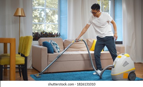 Young Asian Man Cleaning House With Vacuum Cleaner. Portrait Of Handsome Korean Guy Vacuuming Blue Carpet In Modern Living Room Doing Household.