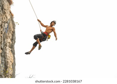 Young Asian man climber climbing on rocky coastline at tropical island in sunny day. Handsome guy enjoy outdoor active lifestyle and extreme sport training mountain climbing on summer holiday vacation - Powered by Shutterstock