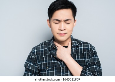 Young Asian Man With Closed Eyes Touching Neck While Suffering From Sore Throat Isolated On Grey