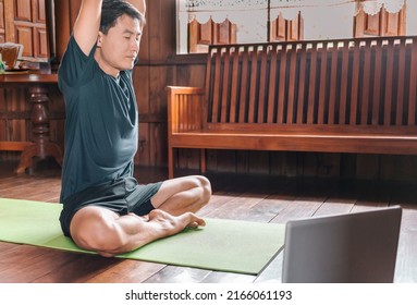 Young Asian Man  Coach Internet Video Online Training Yoga Instructor Modern Laptop Screen Meditate Sukhasana Posture Relax Breathe Easy Seat Pose Gym Healthy Lifestyle At Home Concept.