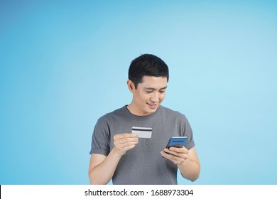 Young Asian Man With Credit Card Doing Online Transaction Buy, Purchase Or Sell Stuff, In Studio Isolated Gray Background