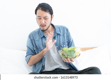 Young Asian Man Does Not Want To Eat And Has No Appetite Not Eat Salad. Adult Man Do Not Like To Eat Vegetables, Healthy Food, Vegetarian Products. Negative Displeased Face Expression.