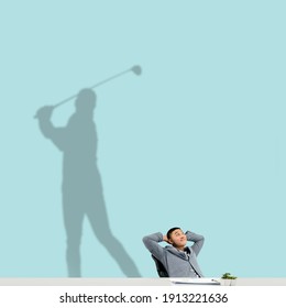 Young Asian Man Dreaming About Future In Big Sport During His Work In Office. Becoming A Legend. Shadow, Silhouette Of Professional Golf Player On The Wall. Inspiration, Aspiration. Copyspace.