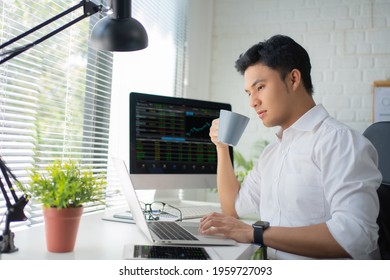 Young Asian man drinking coffee while looking at a monitor with financial information in the office. Online Trading Concepts. - Powered by Shutterstock