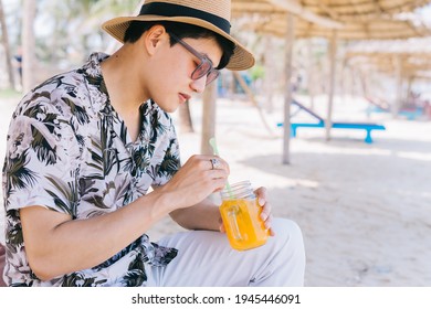 Young Asian Man Drinking Orange Juice On The Beach