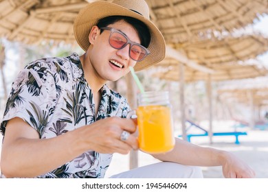 Young Asian Man Drinking Orange Juice On The Beach