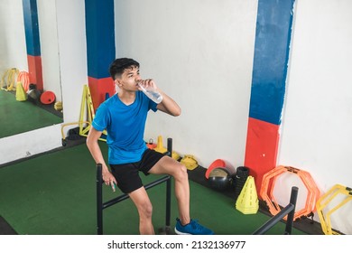 A young asian man drinks a bottle of water after a set of sled pushes at the gym. Cooling off after an intense workout. - Powered by Shutterstock