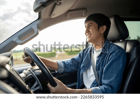 A young Asian man drives a car on a clear day. With beautiful blue sky. He smiling driving to travel by car. Sticking her head outta the windshield