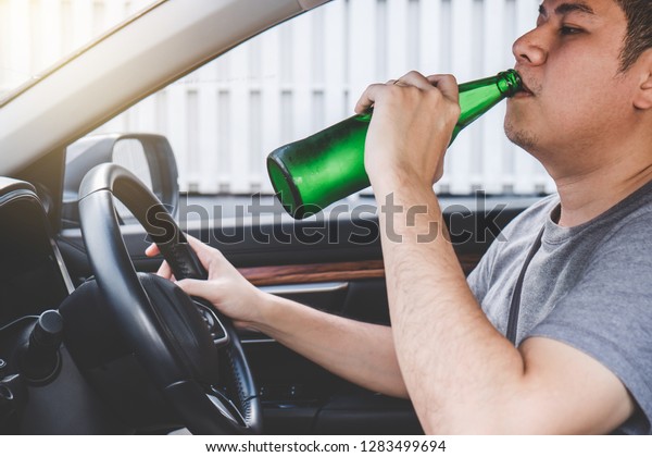 Young asian man drives a car with drunk a
bottle of beer behind the wheel of a
car.