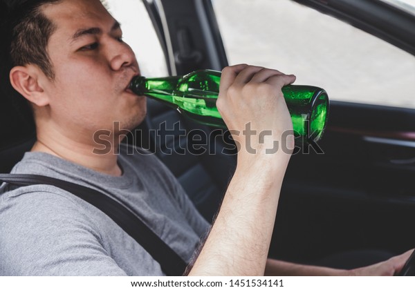 Young asian man drives a car with drunk a\
bottle of beer behind the wheel of a\
car.