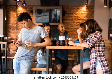 A young asian man excluding himself and checking his phone standing besides his friends. - Shutterstock ID 1865163139