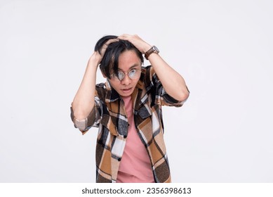 A young asian man freaking out and breaking down from stress. Grabbing his scalp, overwhelmed by pressure. Mental health concept. Isolated on a white background.