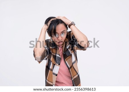 A young asian man freaking out and breaking down from stress. Grabbing his scalp, overwhelmed by pressure. Mental health concept. Isolated on a white background.