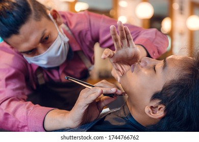 Young Asian Man Getting Shave At The Barbershop. Skilled Barber Shaving With Straight Razor