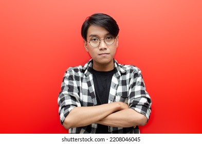 Young Asian Man With Glasses In Casual Black T-shirt And Flanel With Arm Crossed Looking At Camera Shows Good Attitude And Confidence Isolated Over Red Background.millenials With Good Attitude Concept