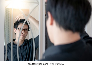 Young Asian Man With Glasses Looking Into The Mirror On Closet While Dressing Up In Bedroom. Home Living Concept