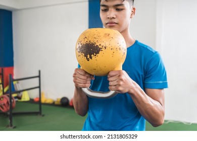 A young asian man grasps firmly an old rusted kettlebell. Holding upside-down. Preparing to do a set of goblet squats. Working our at the gym.