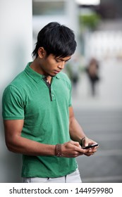 Young Asian Man In Green Polo Shirt Is Texting On His Cell Phone