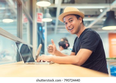 Young asian man with hat using laptop and showing thumb up