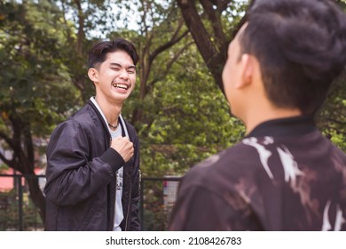 A young asian man having a lighthearted chat with his friend. Outdoor park scene. - Shutterstock ID 2108426783