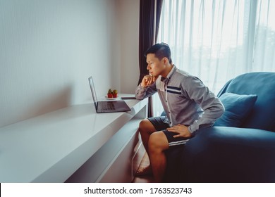 Young Asian Man Having Video Conference Meeting With Boxer Shorts On Sofa At Home During Quarantine.