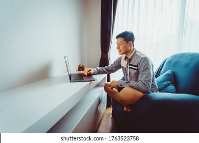 Young Asian Man Having Video Conference Meeting With Boxer Shorts On Sofa At Home During Quarantine.