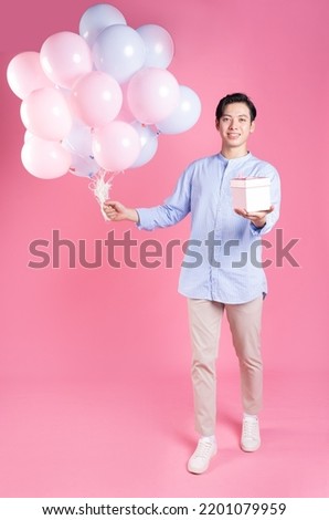 Young Asian man holding balloon on pink background