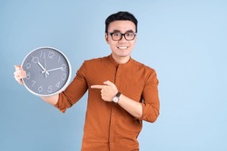 Young Asian Man Holding Clock On Blue Background