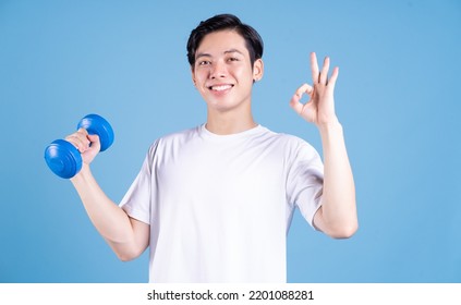 Young Asian man holding dumbbell on background - Powered by Shutterstock