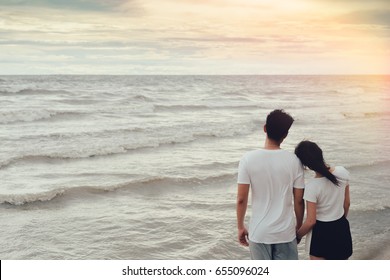 Young asian man holding hand with girl romantic together relationship valentine lover day at beach vacation time leisure back view  sunset evening.