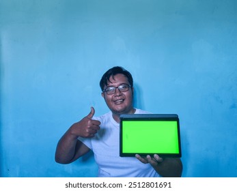 Young Asian man  holding and pointing at an  tablet green screen mockup - Powered by Shutterstock