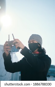 Young Asian Man Holding  Radio Remote Controller On The Street. Boy Flying A Drone Outside At Daytime. Quadcopter Operator Standing In Sunlight With Face Mask. Shallow Depth Of Field.