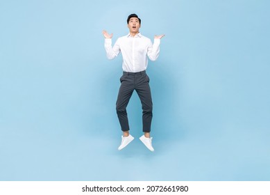 Young Asian Man Jumping With Open Palms And Looking Up In Isolated Light Blue Color Background