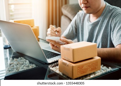 Young asian man looking on computer laptop and writing order list on paper, SME concept.