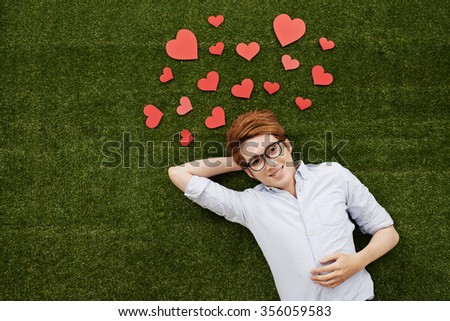 Young Asian man in love lying on green grass and looking at the camera